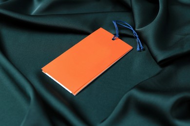 Photo of Blank orange tags on green silky fabric, closeup. Space for text