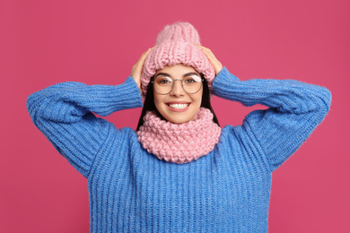 Photo of Young woman wearing warm sweater, snood and hat on crimson background. Winter season