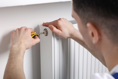 Professional repairman fixing heating radiator with pliers indoors, closeup