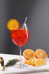 Glass of tasty Aperol spritz cocktail with orange slices and rosemary on white table against gray background