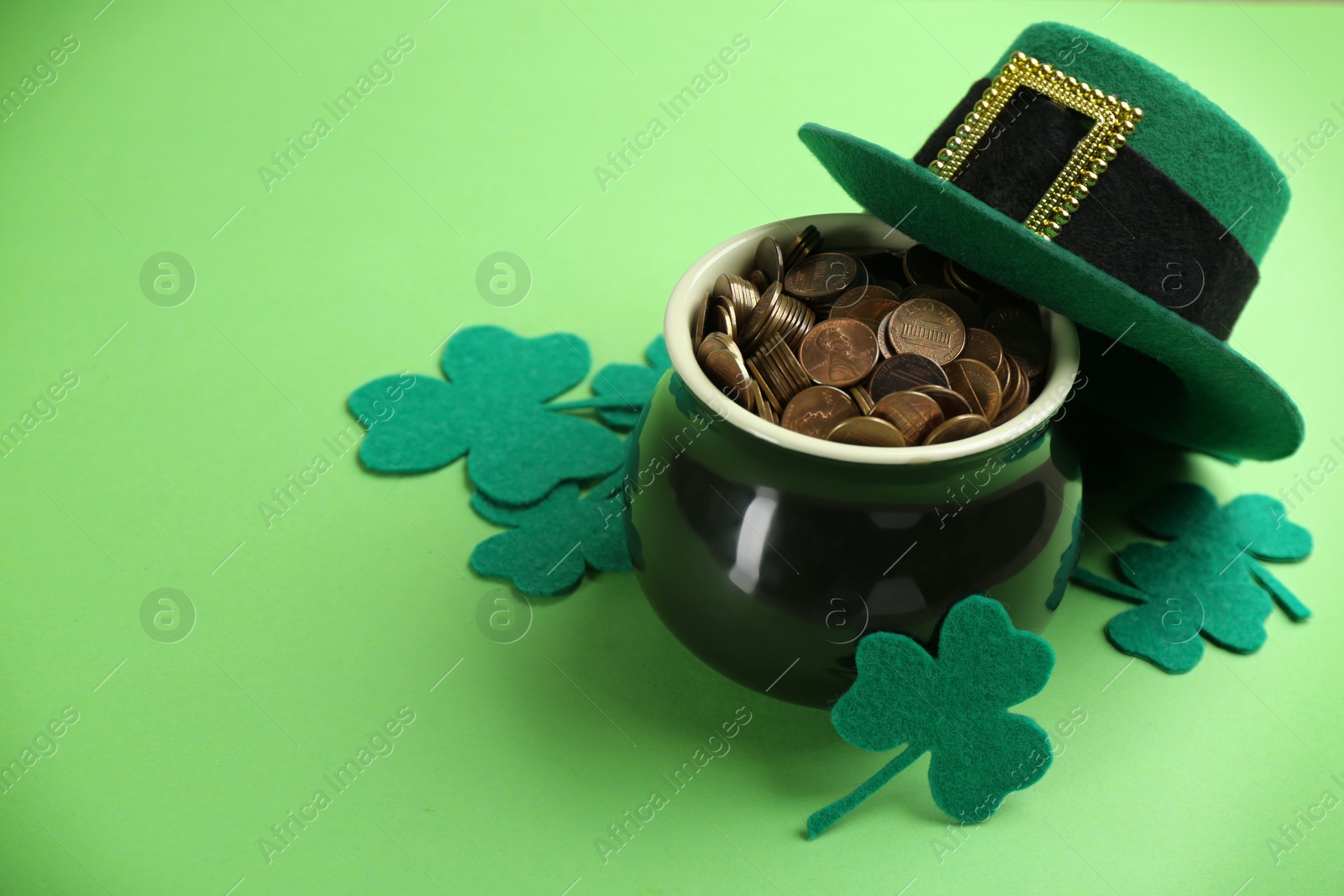 Photo of Pot of gold coins, hat and clover leaves on green background, space for text. St. Patrick's Day celebration