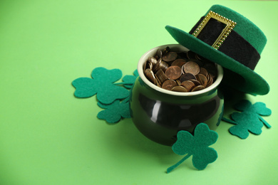 Photo of Pot of gold coins, hat and clover leaves on green background, space for text. St. Patrick's Day celebration