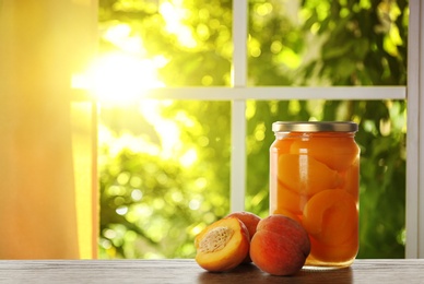 Image of Jar of tasty pickled peaches on wooden table in kitchen. Space for text