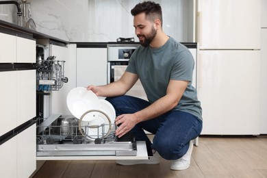 Photo of Smiling man loading dishwasher with plates in kitchen