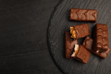 Slate plate of chocolate bars with caramel, nuts and nougat on black table, top view. Space for text