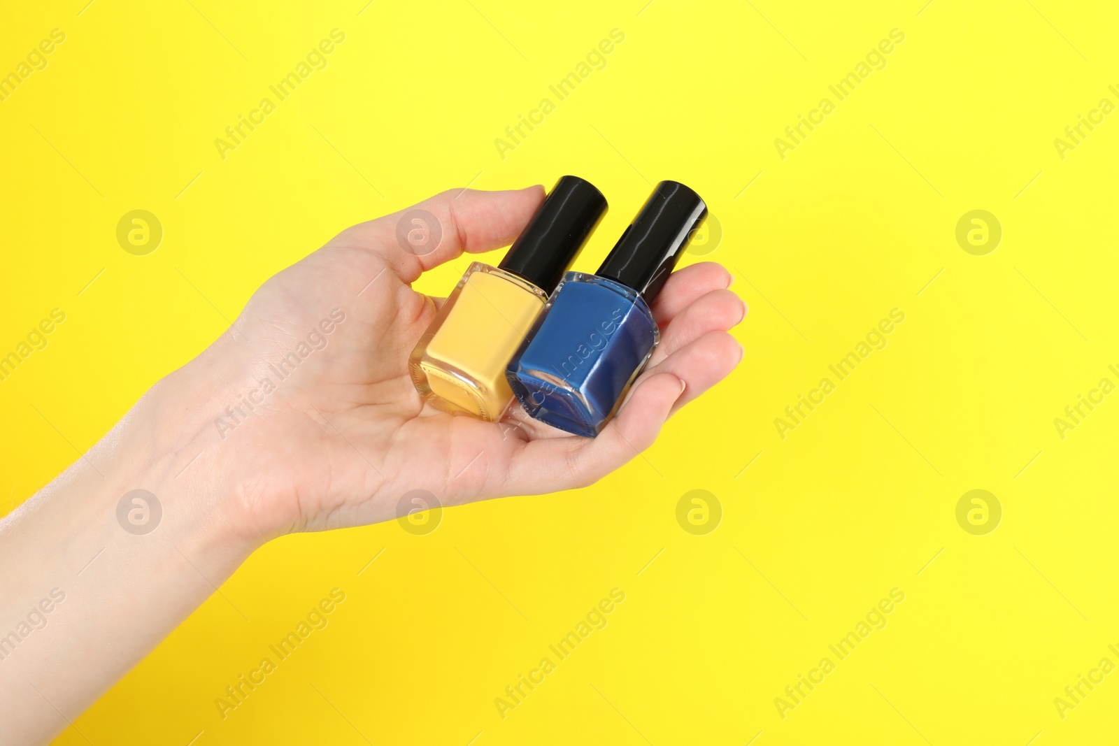 Photo of Woman holding nail polishes on yellow background, closeup