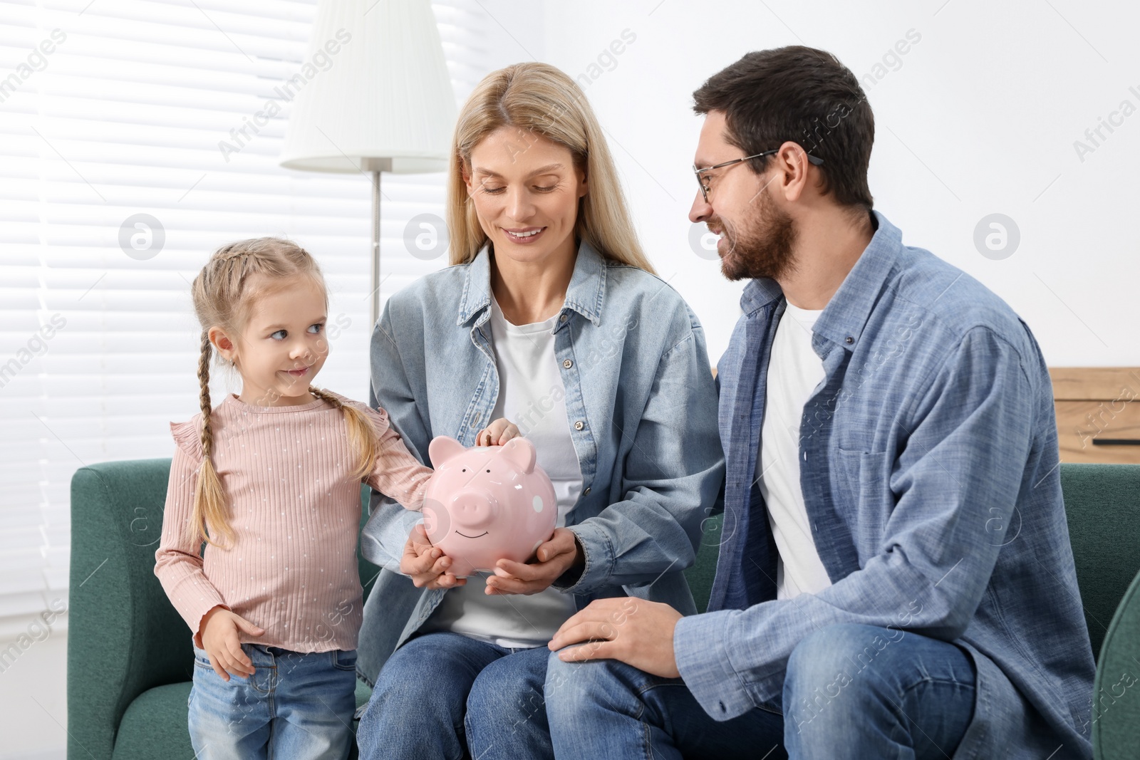 Photo of Planning budget together. Little girl with her parents putting coin into piggybank at home