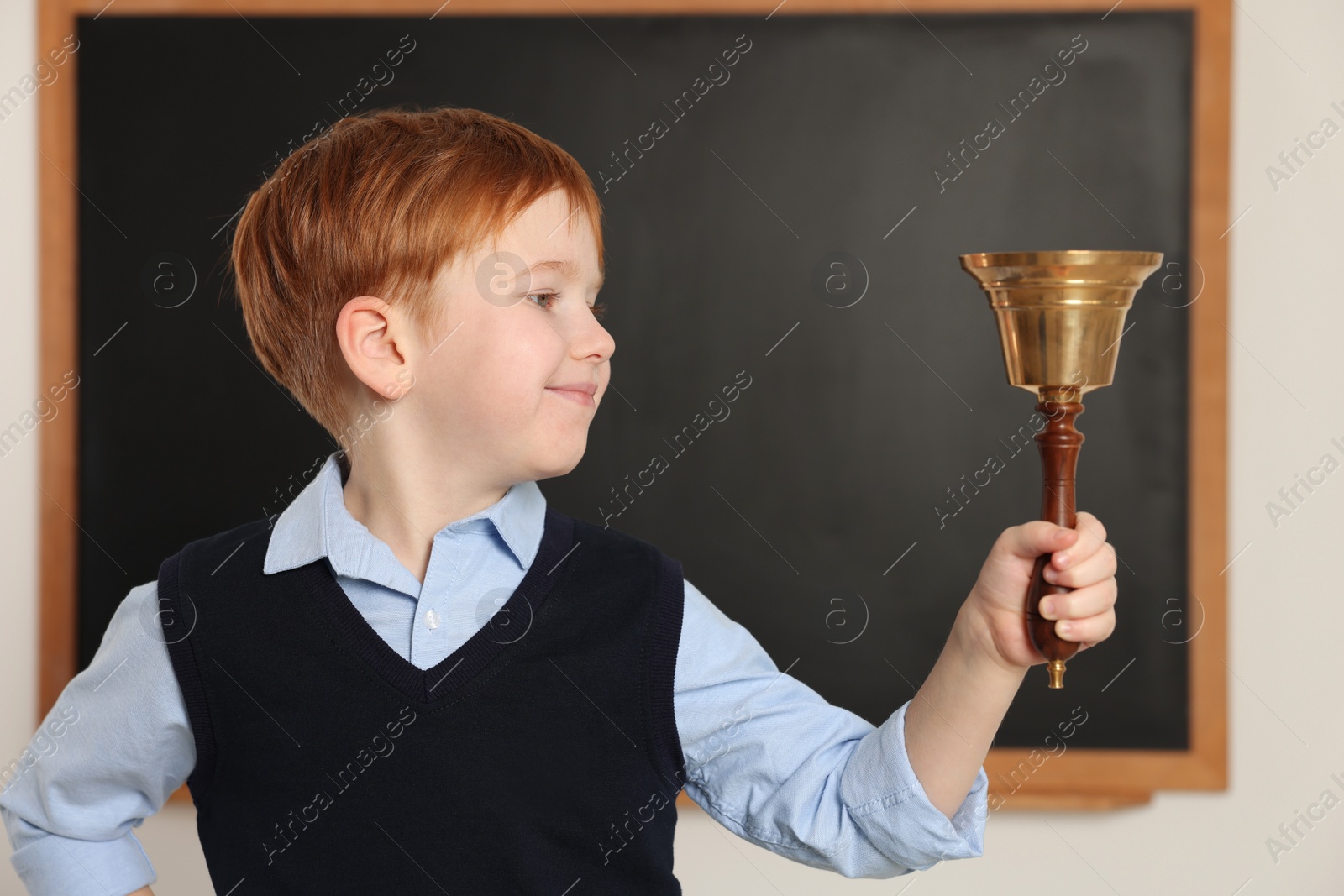 Photo of Cute little boy ringing school bell in classroom