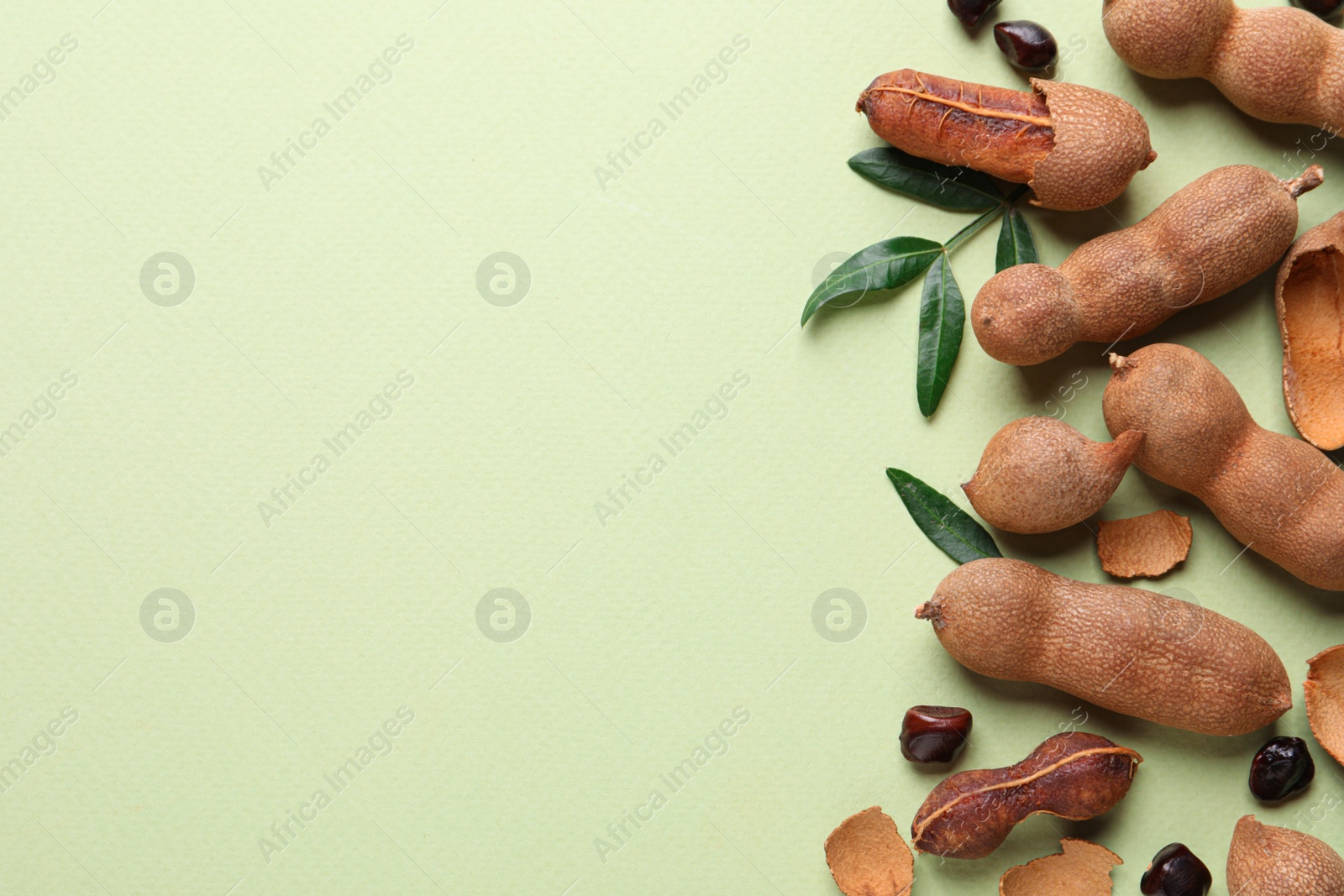 Photo of Ripe tamarinds and fresh leaves on light green background, flat lay. Space for text