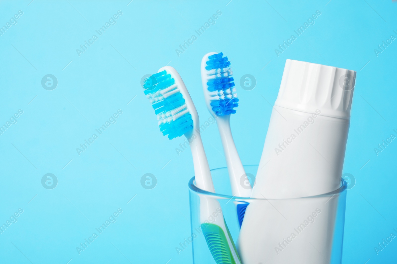 Photo of Glass with brushes and toothpaste on color background. Space for text