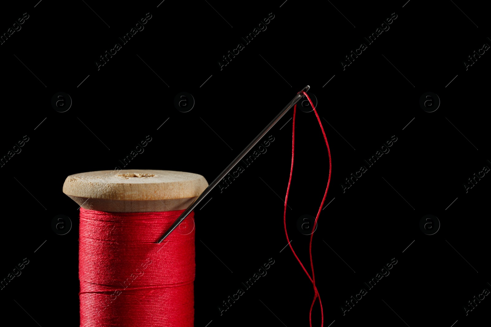 Photo of Red sewing thread with needle on black background, closeup