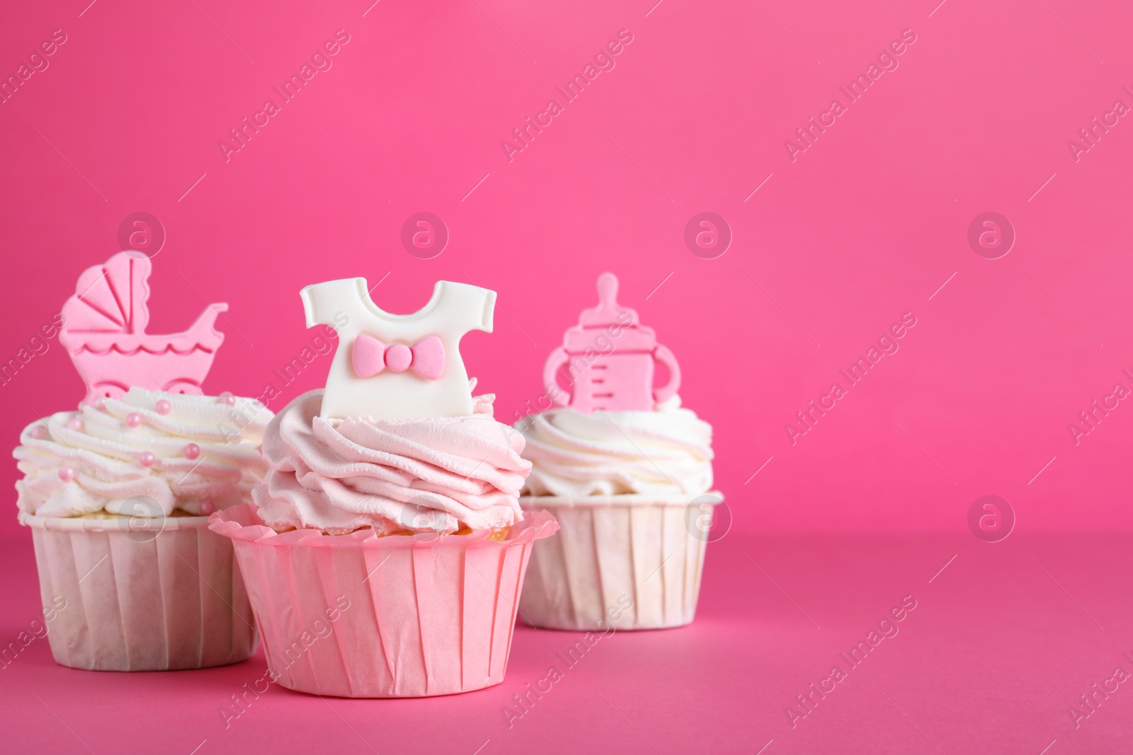 Photo of Beautifully decorated baby shower cupcakes with cream and girl toppers on pink background. Space for text