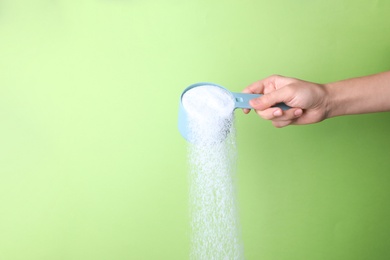 Woman pouring laundry detergent from measuring container against green background, closeup. Space for text