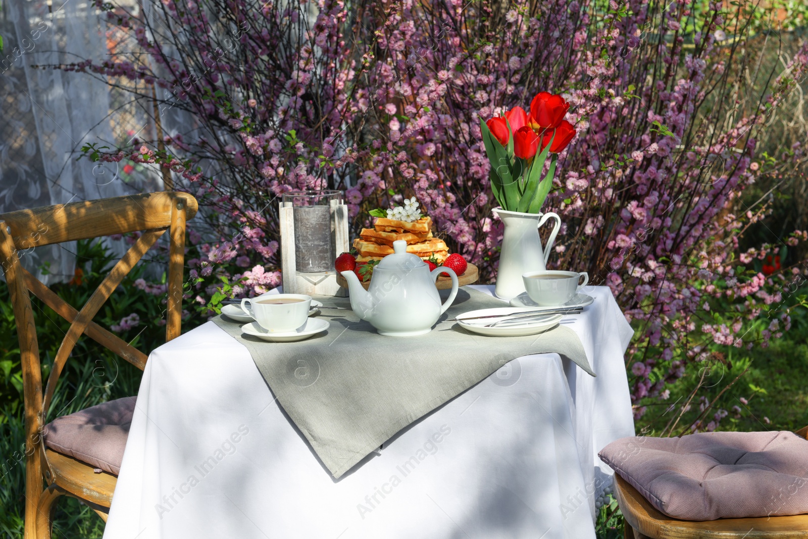 Photo of Beautiful bouquet of tulips and freshly baked waffles on table served for tea drinking in garden