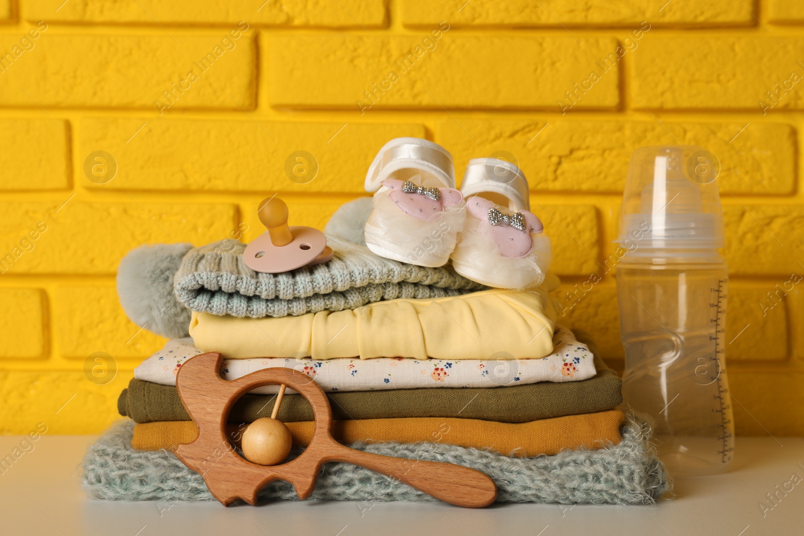 Photo of Baby clothes, toy and accessories on white table near yellow brick wall