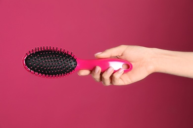 Photo of Woman holding hair brush against crimson background, closeup