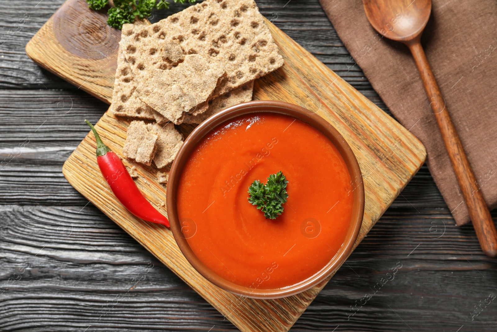 Photo of Board with bowl of fresh homemade tomato soup and crispbreads on wooden background, top view