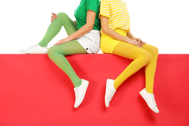 Photo of Women wearing bright tights sitting together on color background, closeup