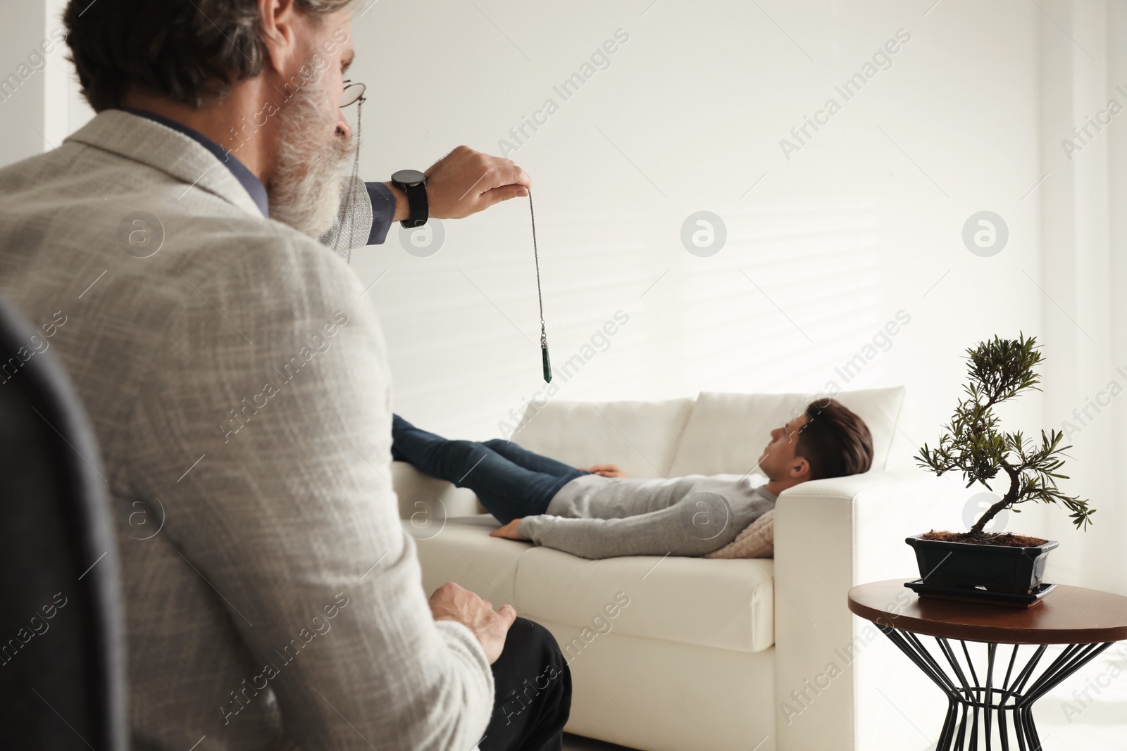 Photo of Psychotherapist using pendulum during hypnotherapy   session in office