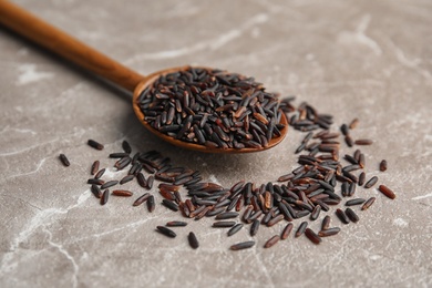 Spoon with uncooked black rice on grey background