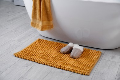 Photo of Soft orange mat and slippers on floor near tub in bathroom. Interior design