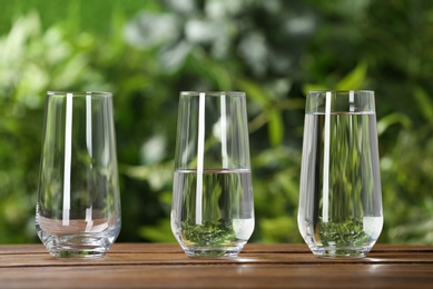 Empty, half and full glasses of water on wooden table against blurred background