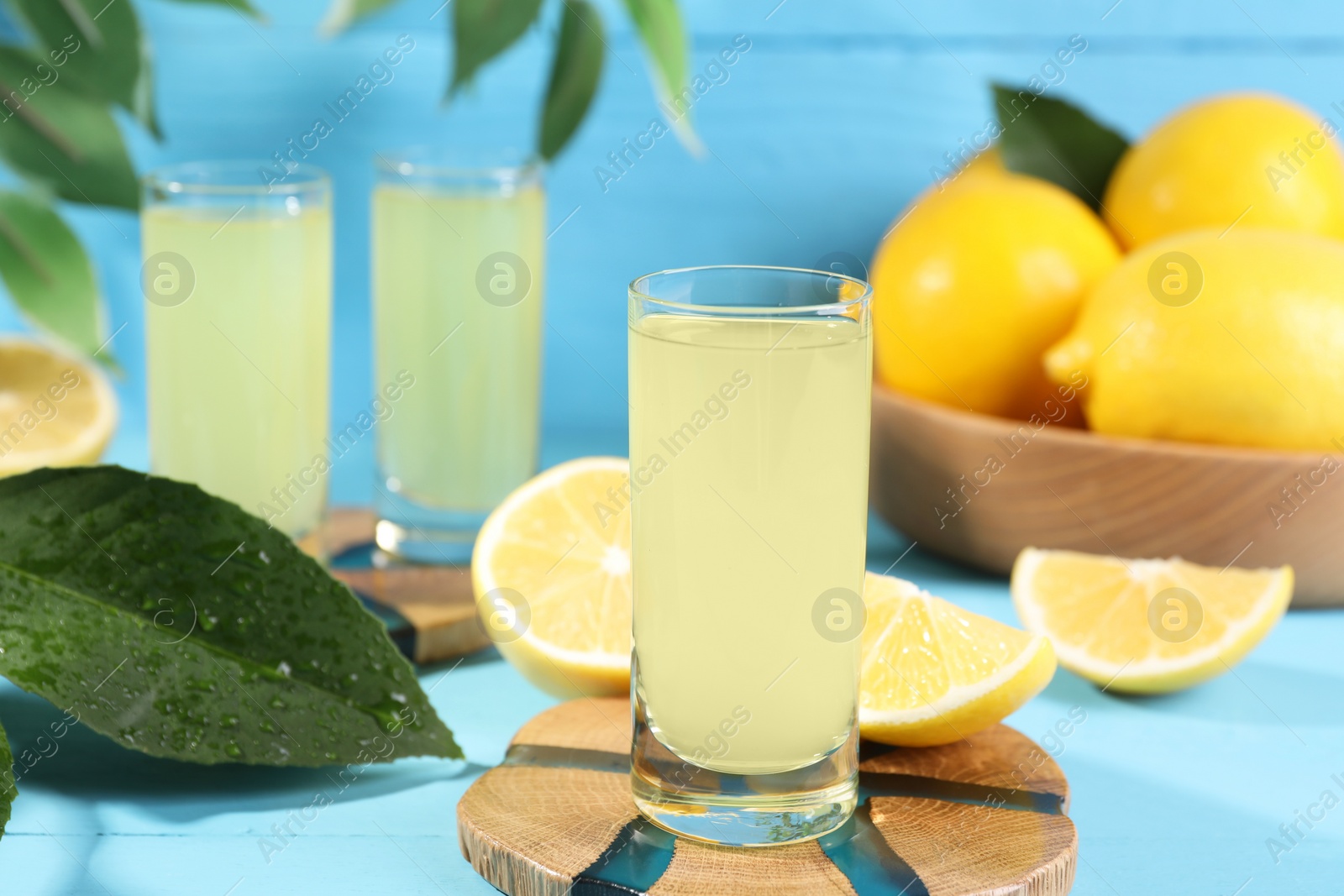 Photo of Tasty limoncello liqueur, lemons and green leaves on light blue table