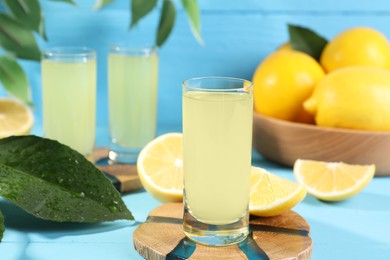 Photo of Tasty limoncello liqueur, lemons and green leaves on light blue table