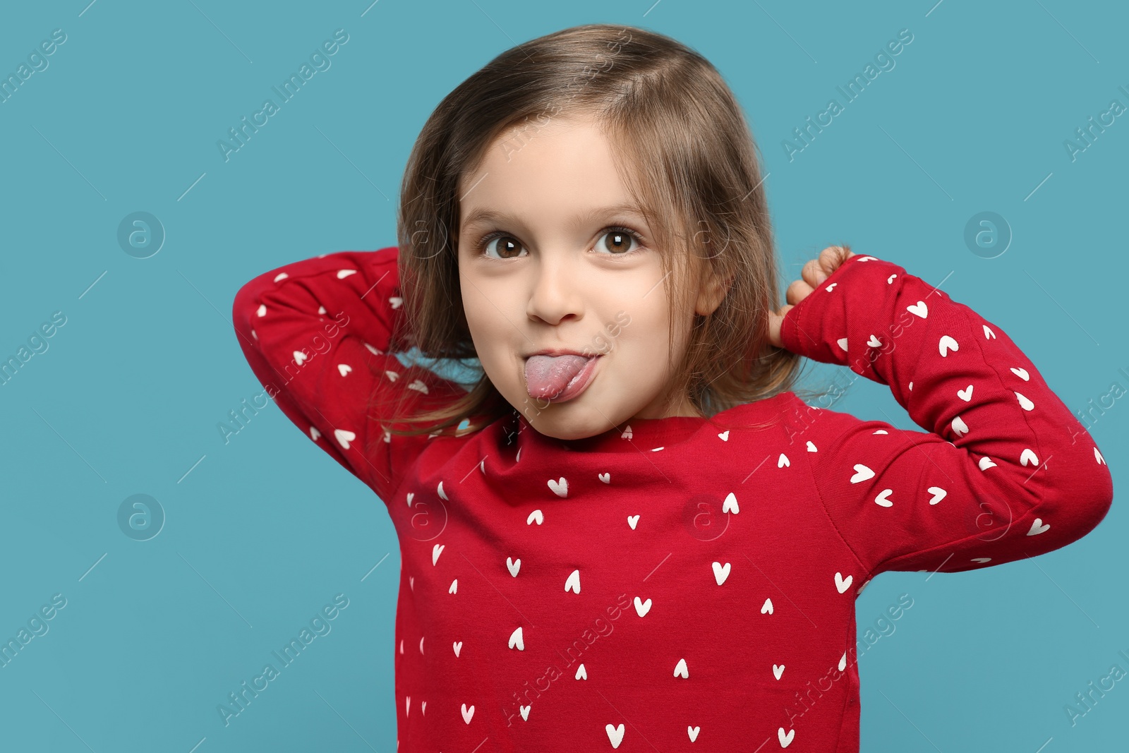 Photo of Funny little girl showing her tongue on light blue background