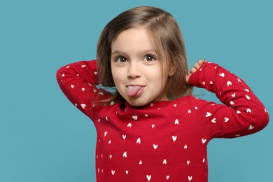 Photo of Funny little girl showing her tongue on light blue background