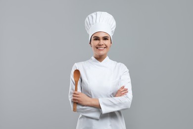 Photo of Happy female chef with wooden spoon on light grey background
