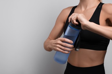 Photo of Sportswoman with bottle of water on light grey background, closeup. Space for text