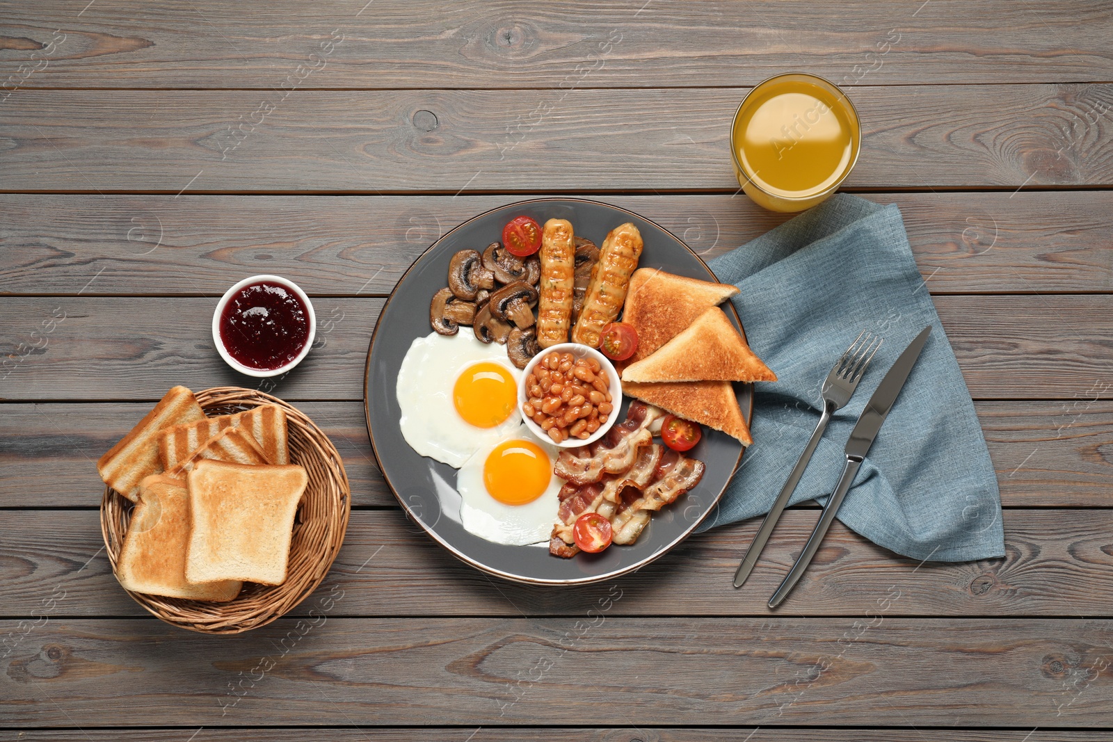 Photo of Plate of fried eggs, mushrooms, beans, tomatoes, bacon, sausages and toasts served on wooden table, flat lay. Traditional English breakfast