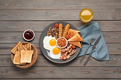 Photo of Plate of fried eggs, mushrooms, beans, tomatoes, bacon, sausages and toasts served on wooden table, flat lay. Traditional English breakfast