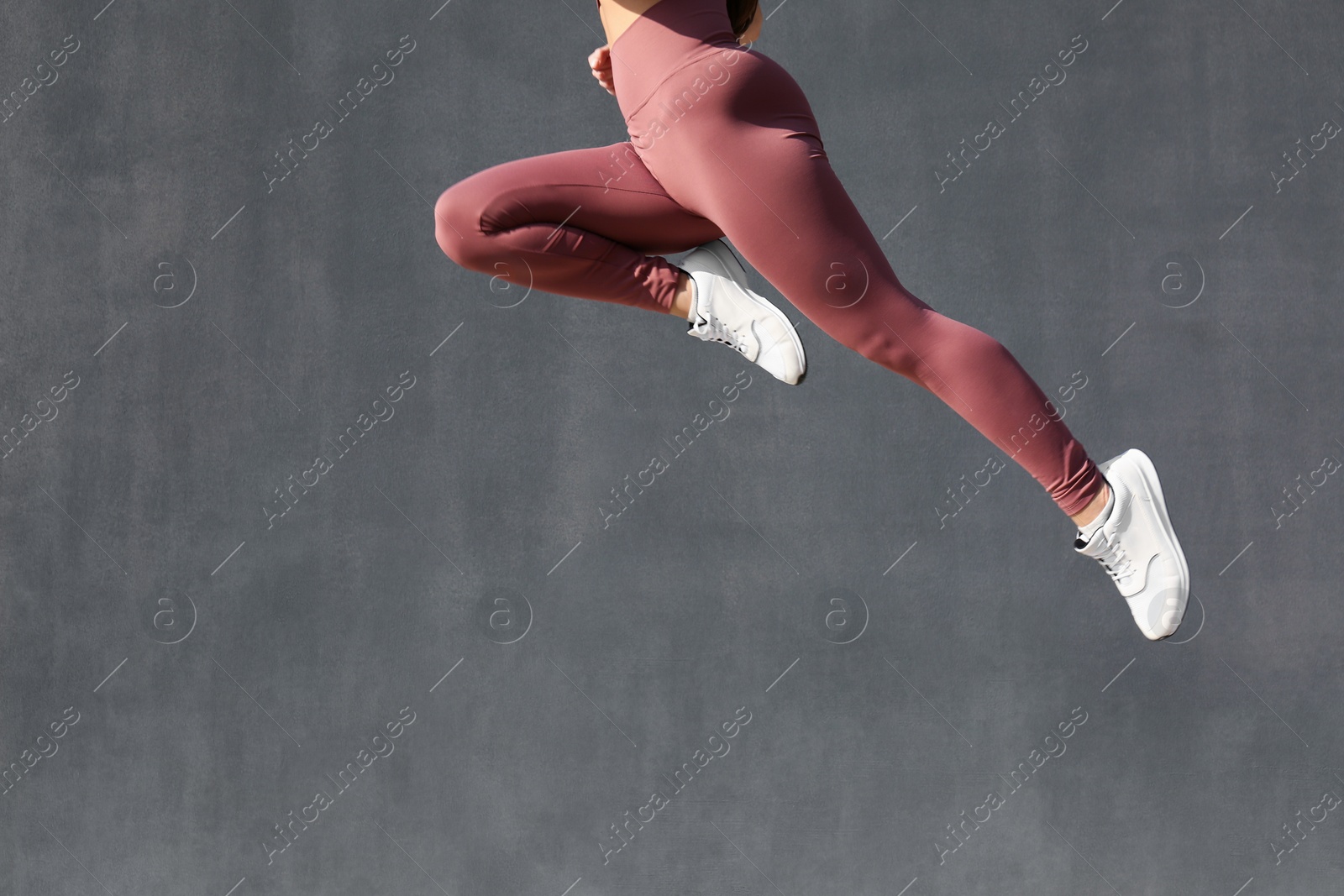 Photo of Young woman in stylish sports wear jumping on grey background, closeup