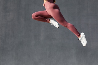 Young woman in stylish sports wear jumping on grey background, closeup