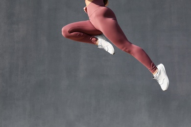 Photo of Young woman in stylish sports wear jumping on grey background, closeup