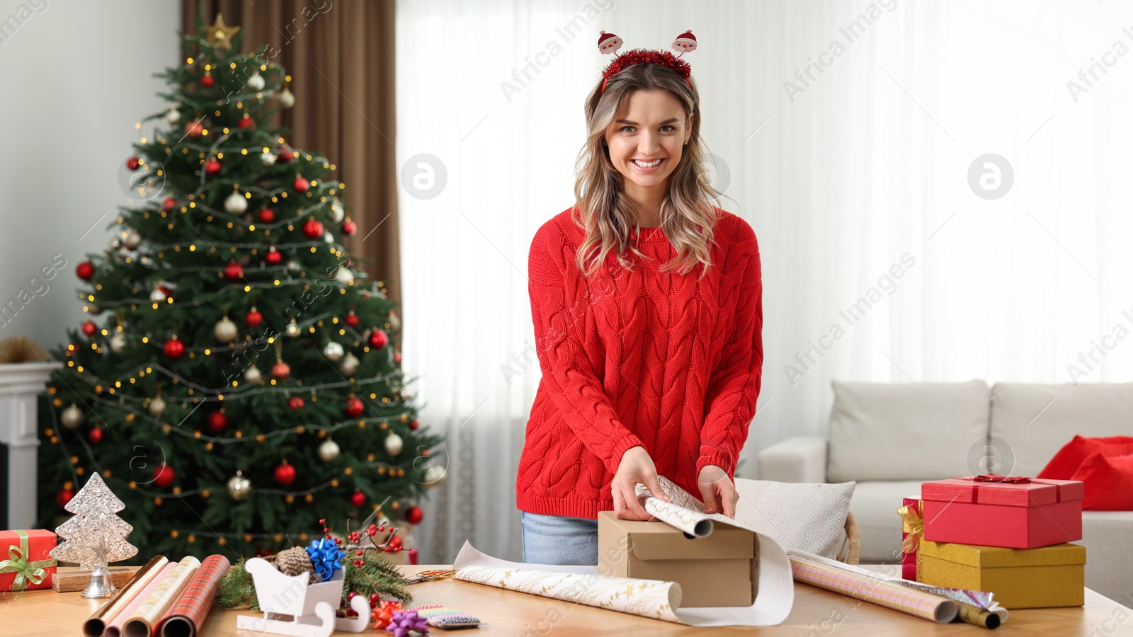 Photo of Beautiful young woman wrapping Christmas gift at home