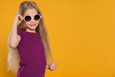 Girl wearing stylish sunglasses on orange background, space for text