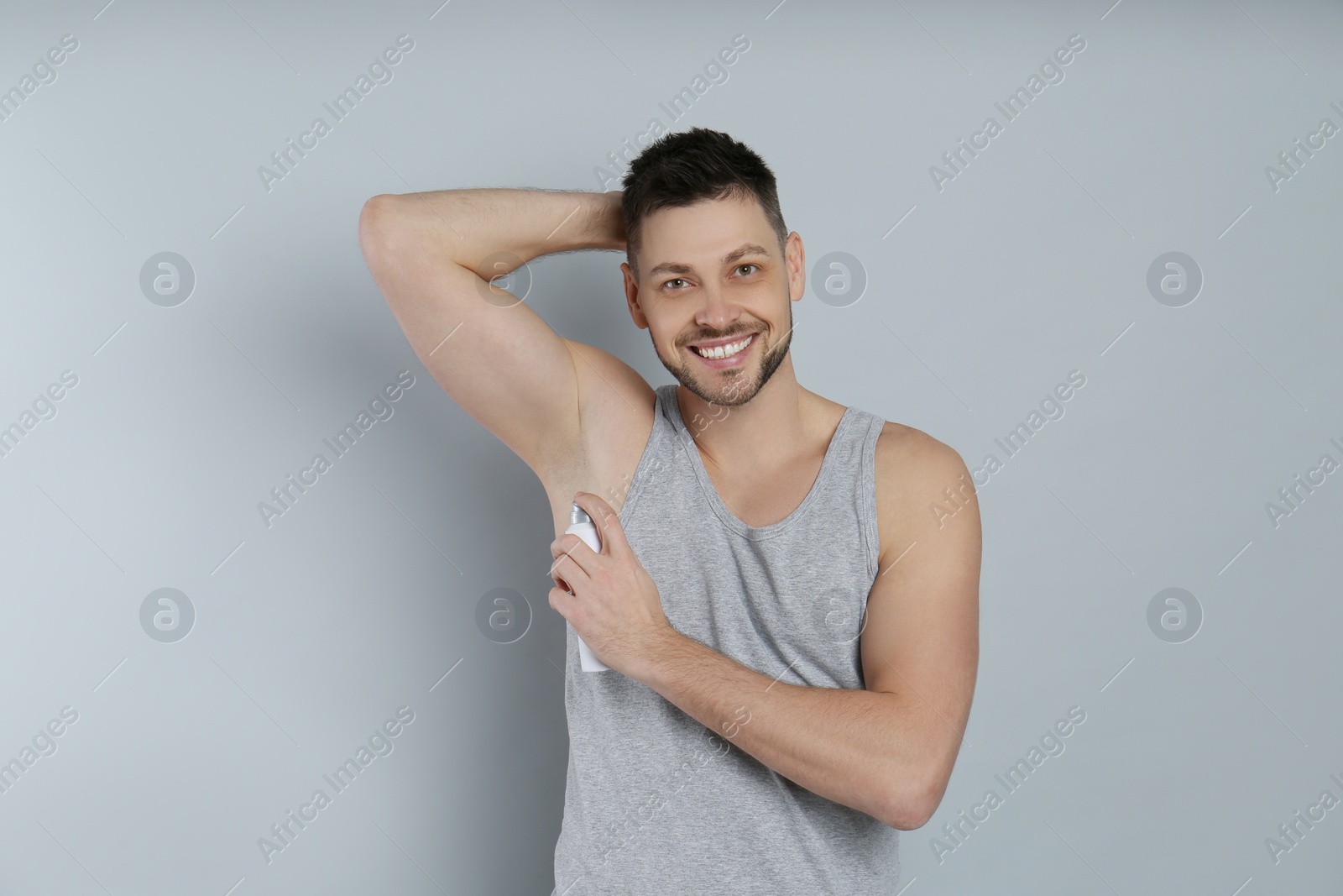 Photo of Handsome man applying deodorant on grey background