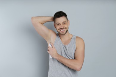 Handsome man applying deodorant on grey background