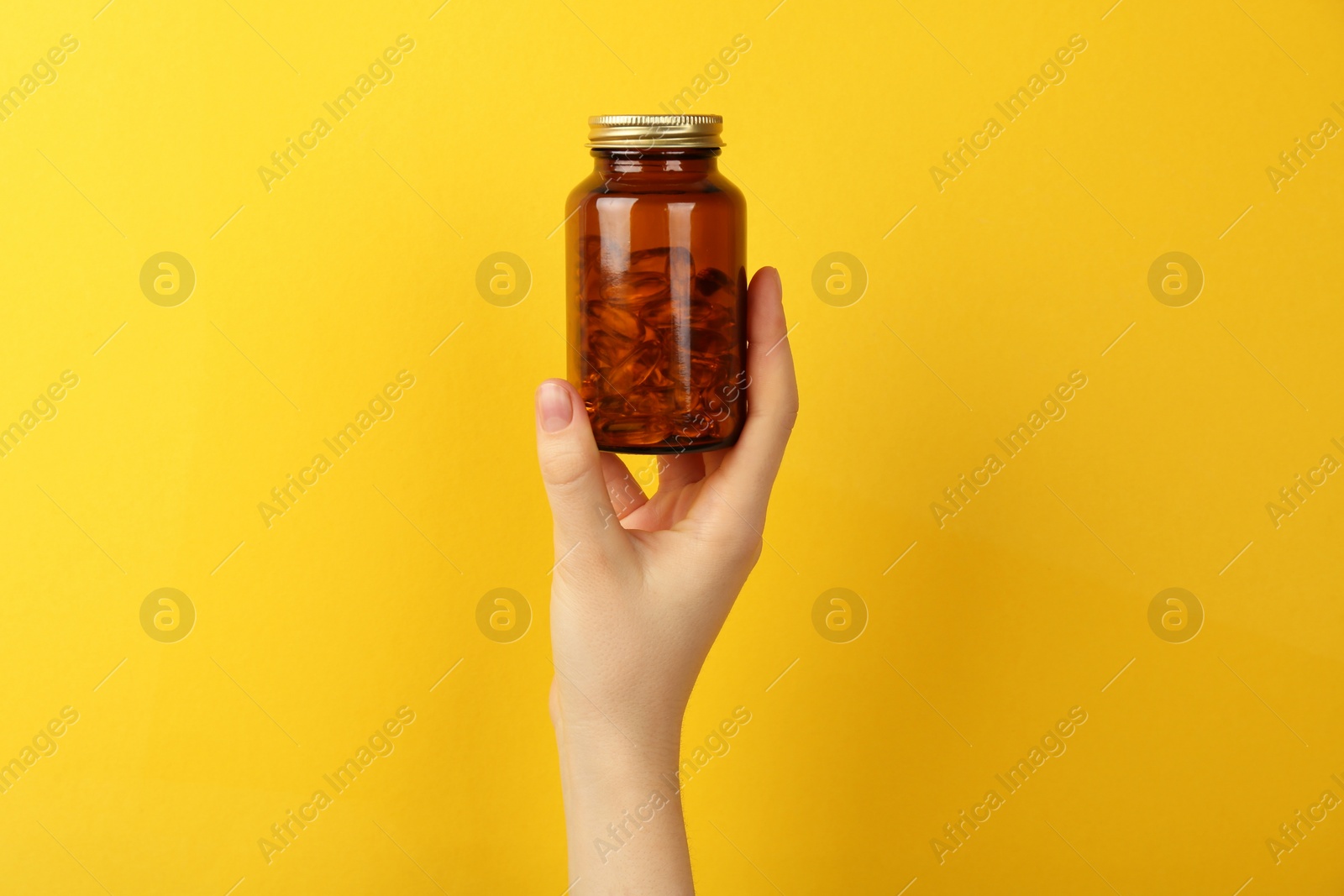 Photo of Woman holding jar with vitamin capsules on yellow background, closeup