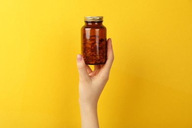 Photo of Woman holding jar with vitamin capsules on yellow background, closeup