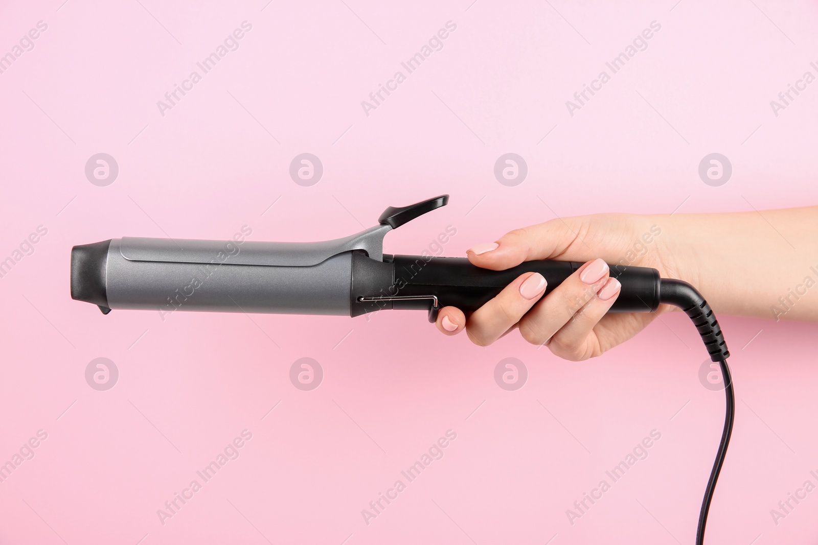 Photo of Hair styling appliance. Woman holding curling iron on pink background, closeup