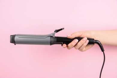 Hair styling appliance. Woman holding curling iron on pink background, closeup