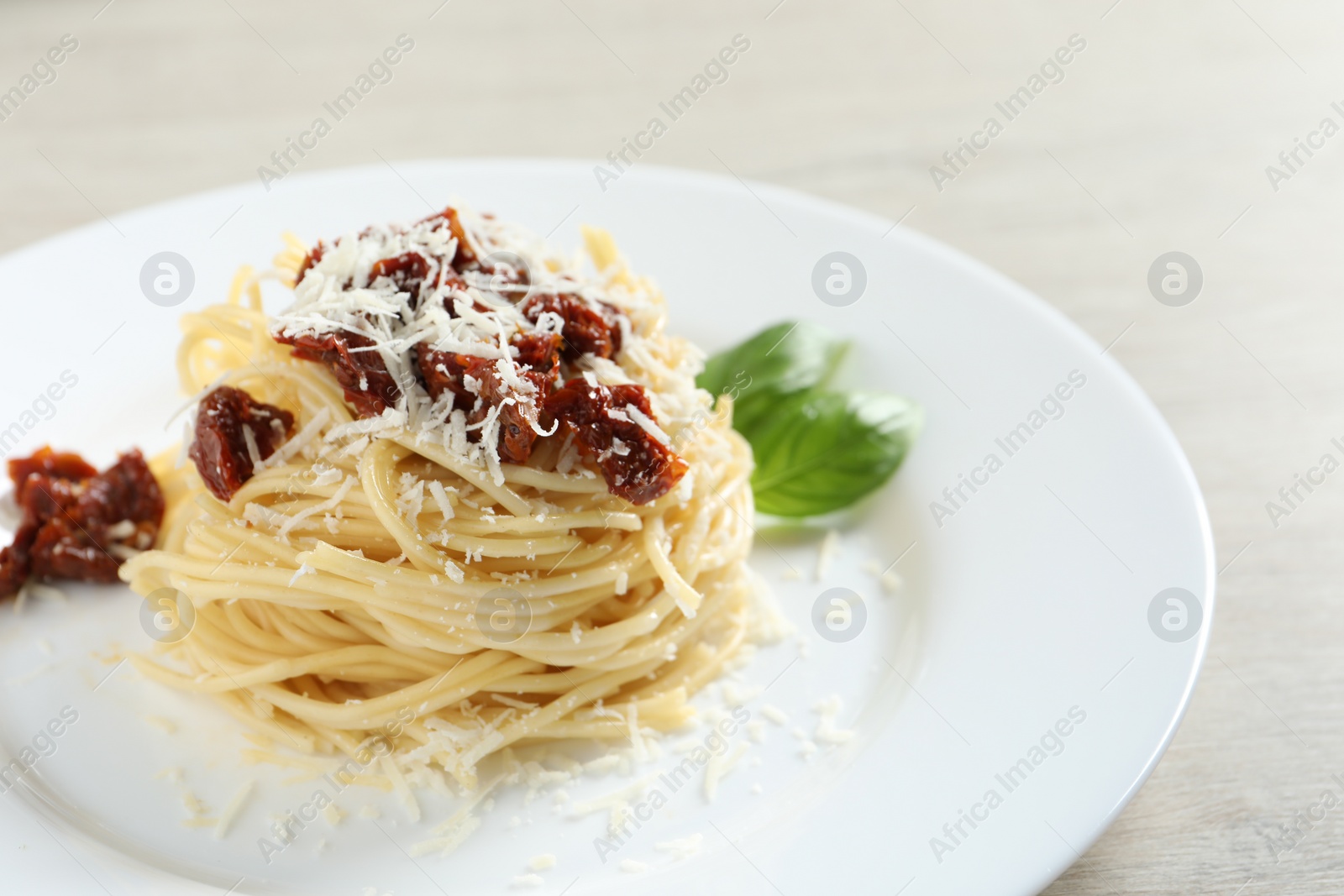 Photo of Tasty spaghetti with sun-dried tomatoes and parmesan cheese on wooden table, closeup. Exquisite presentation of pasta dish