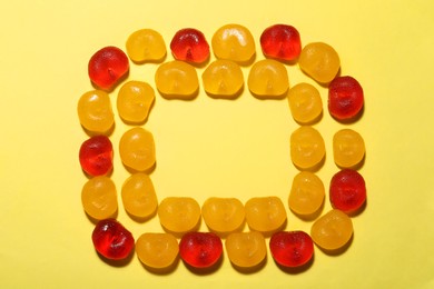 Photo of Frame of delicious gummy cherry candies on yellow background, flat lay. Space for text