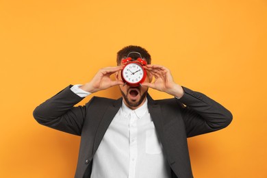 Emotional man with alarm clock on orange background. Being late concept