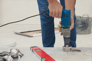 Photo of Worker making socket hole in tile indoors, closeup