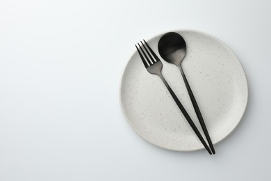 Photo of Plate, fork and spoon on white background, top view. Space for text